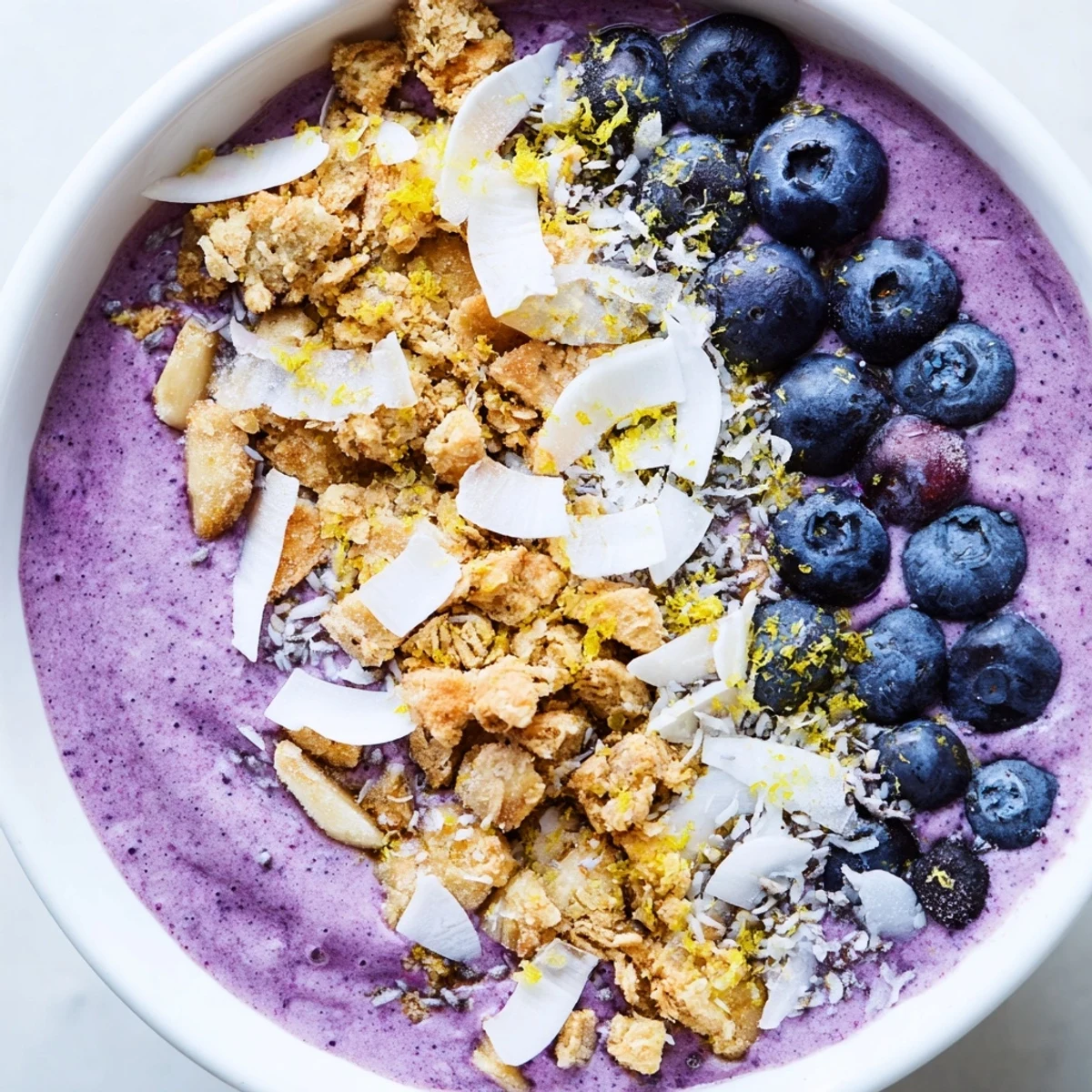 A close-up view of a creamy Lemon Blueberry Smoothie Bowl, showing its rich purple hue and sprinkled chia seeds and lemon zest.