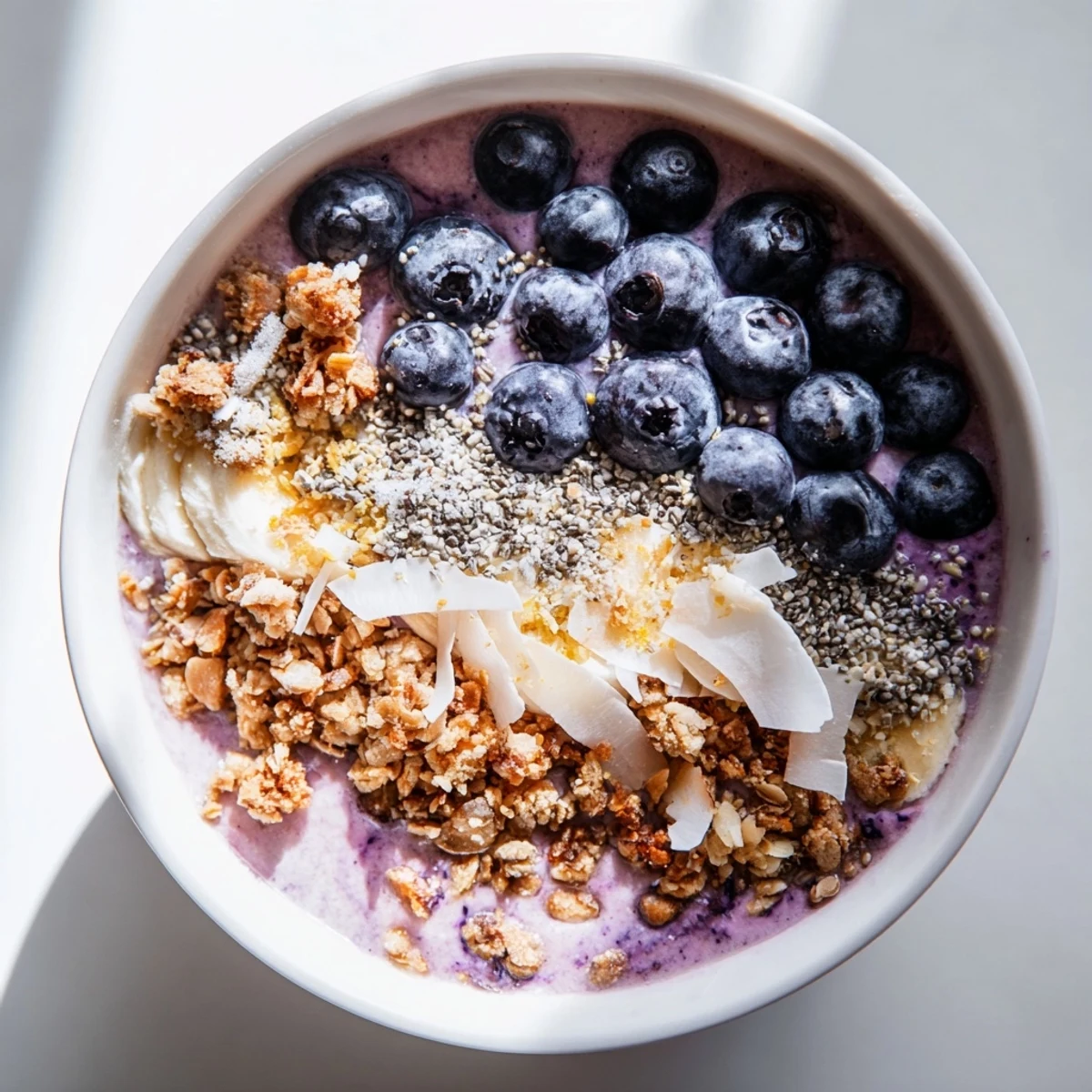 Enjoy this refreshing Lemon Blueberry Smoothie Bowl, a perfect dairy-free and gluten-free snack served with almond milk and crunchy granola.