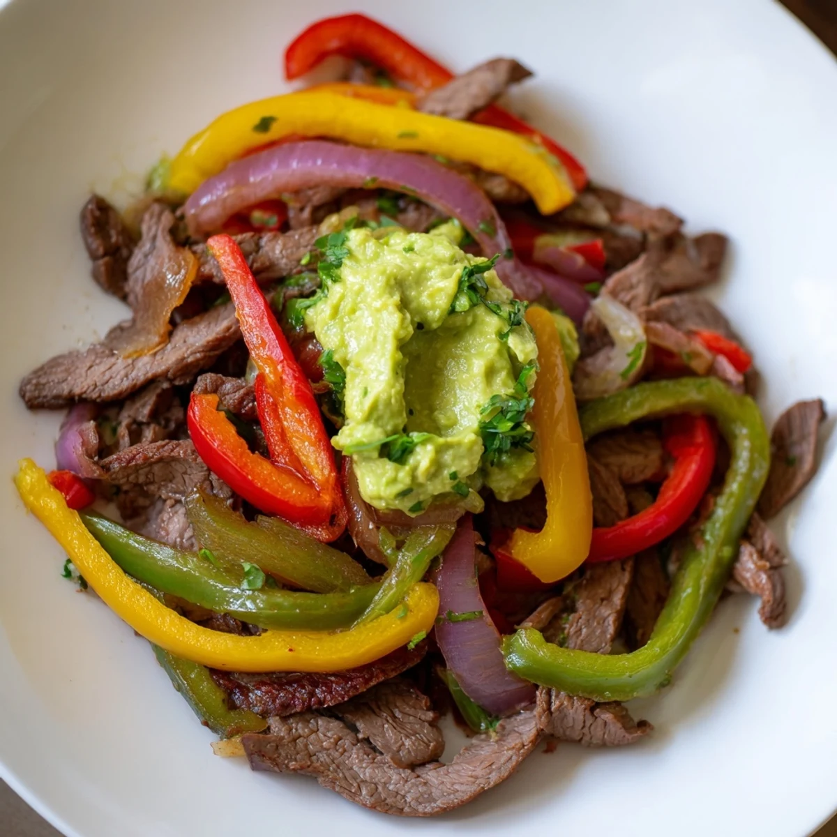 Sizzling strips of marinated beef, sautéed peppers, and onions piled into warm tortillas topped with creamy guacamole in this Beef Fajitas with Guacamole recipe.