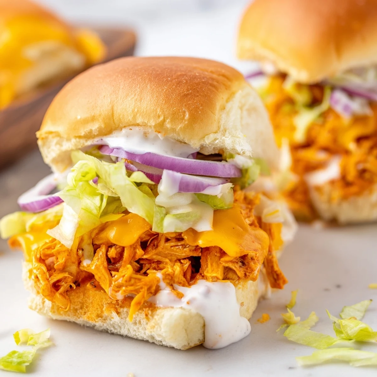 Golden slider buns cradle spicy shredded Buffalo chicken, crunchy veggies, and tangy ranch, creating a savory mini sandwich perfect for casual gatherings and snack platters.