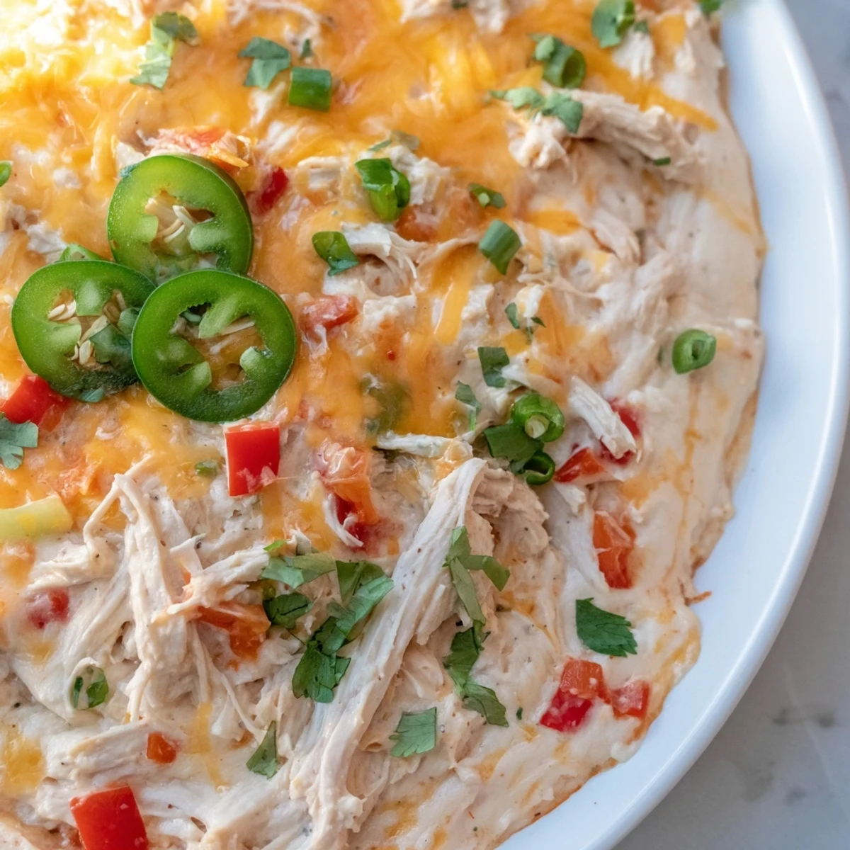 Fresh cilantro and jalapeños garnish this creamy Chicken Enchilada Dip in a rustic serving bowl.