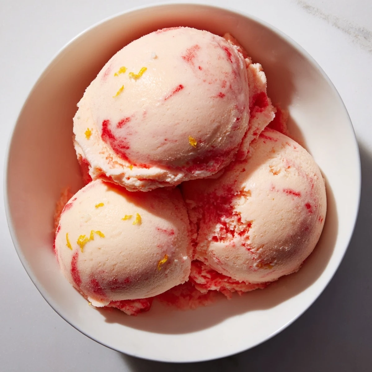 A scoop of vibrant Strawberry Lemonade Sorbet, featuring ruby-red strawberries and bright lemon zest, served in a chilled glass on a warm summer day.  