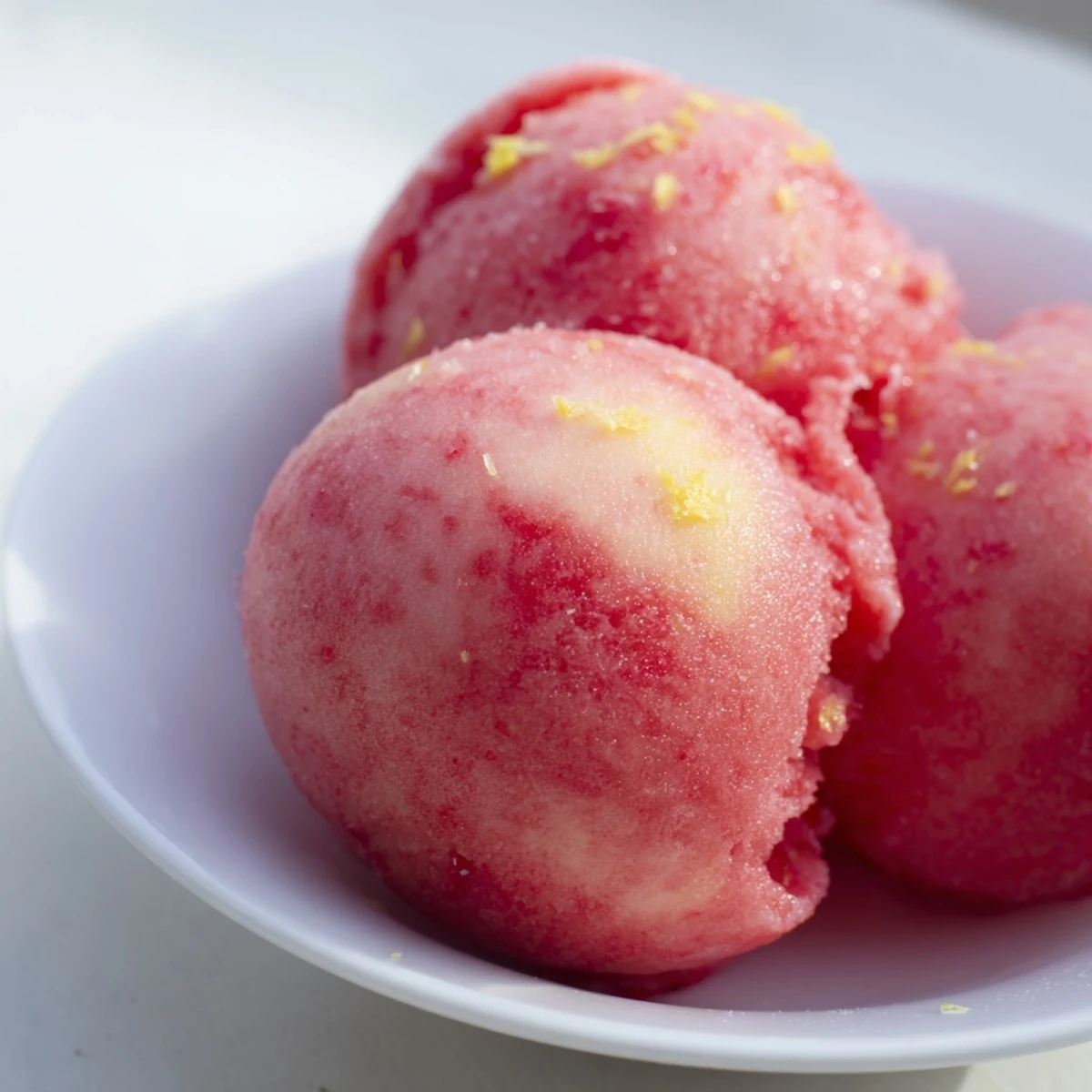 Bright pink Strawberry Lemonade Sorbet in a ceramic bowl, garnished with fresh mint and a lemon wheel, evoking a cool, citrusy summer treat.
