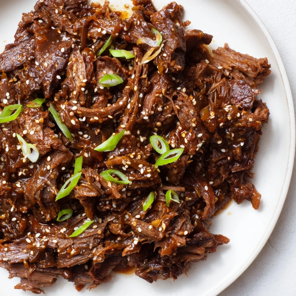 Slow cooker Korean beef simmering in a savory-sweet sauce, garnished with green onions and sesame seeds.