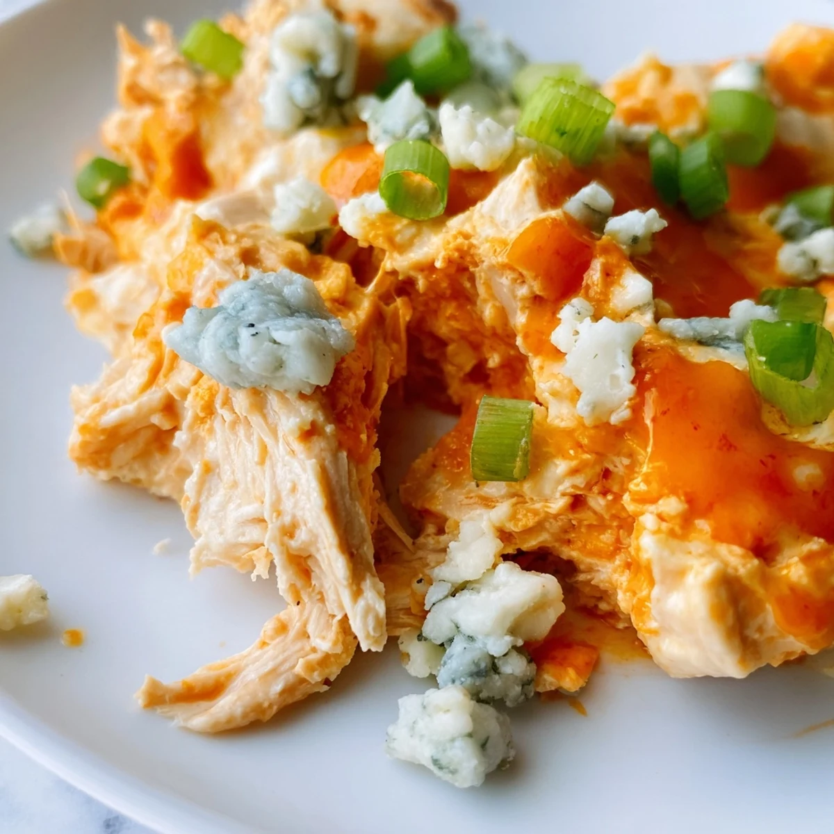 Freshly baked Keto Buffalo Chicken Dip in a ceramic dish, garnished with green onions and blue cheese crumbles. 