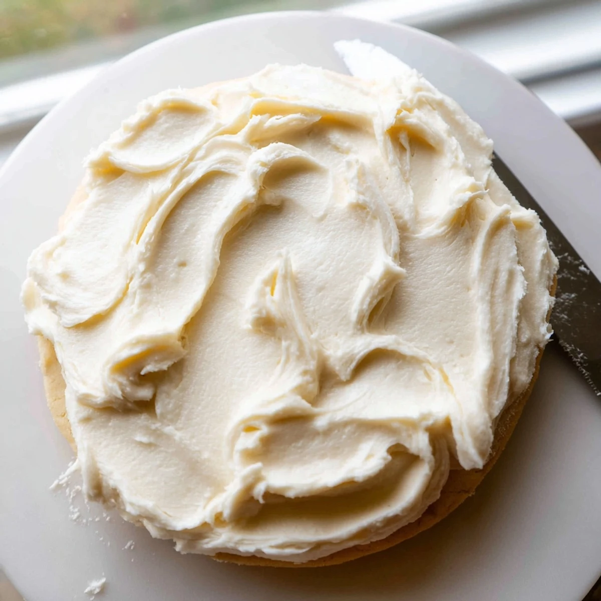 Creamy white Easy Sugar Cookie Frosting swirls onto a freshly baked sugar cookie with a soft, fluffy texture and a hint of vanilla.