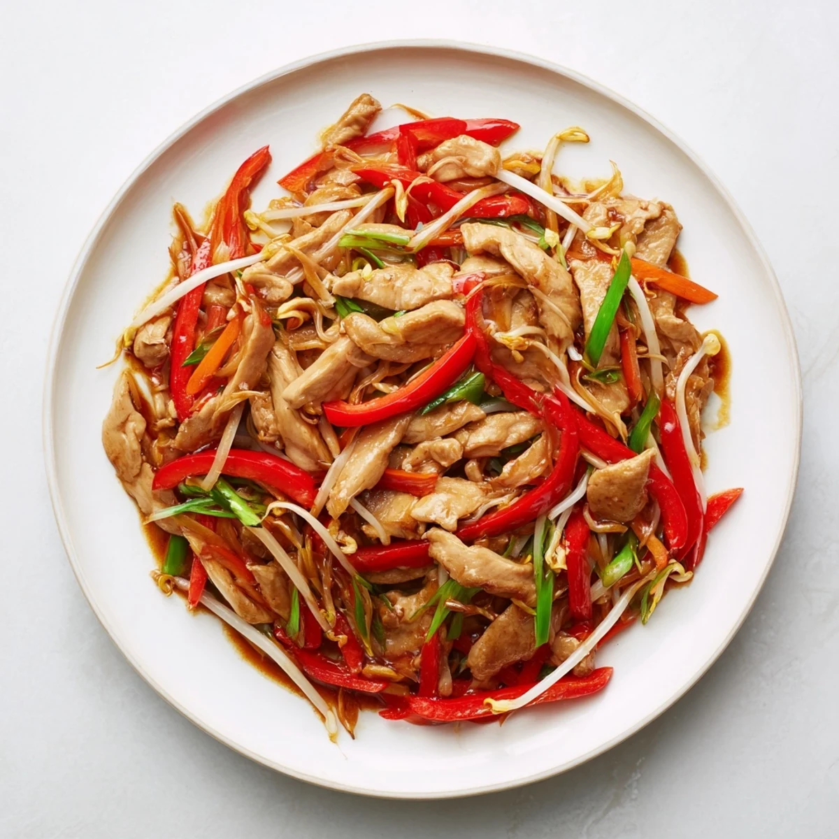 Close-up of Peking Style Chicken stir-fry showing glossy sauce coating crisp bean sprouts and scallions, ready to be served over steamed rice.