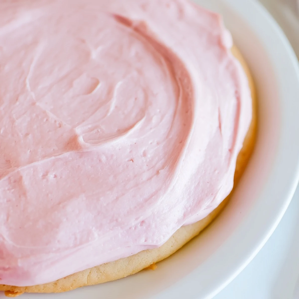 Golden-brown Crumbl Pink Sugar Cookies cooling on a wire rack, each crowned with glossy pink almond frosting.