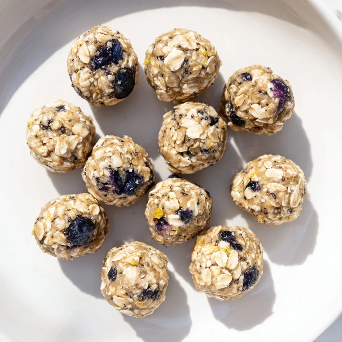 Twelve Blueberry Cheesecake Protein Bites rest on a chilled tray, bursting with fresh blueberries.