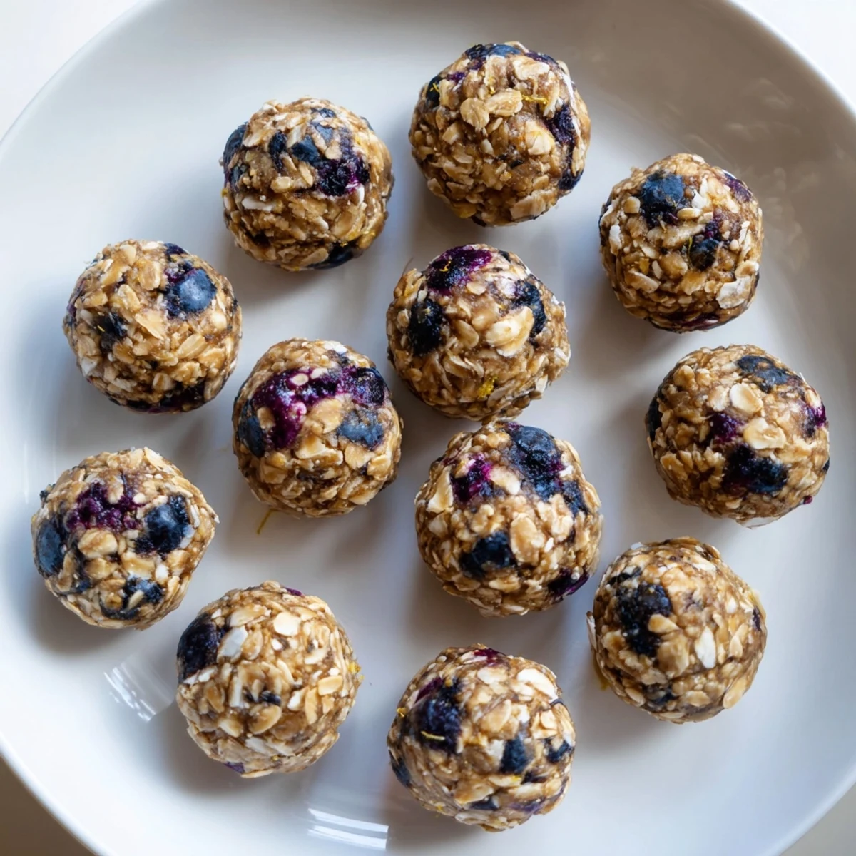 A single Blueberry Cheesecake Protein Bite rests on a spoon, highlighting its no-bake simplicity.