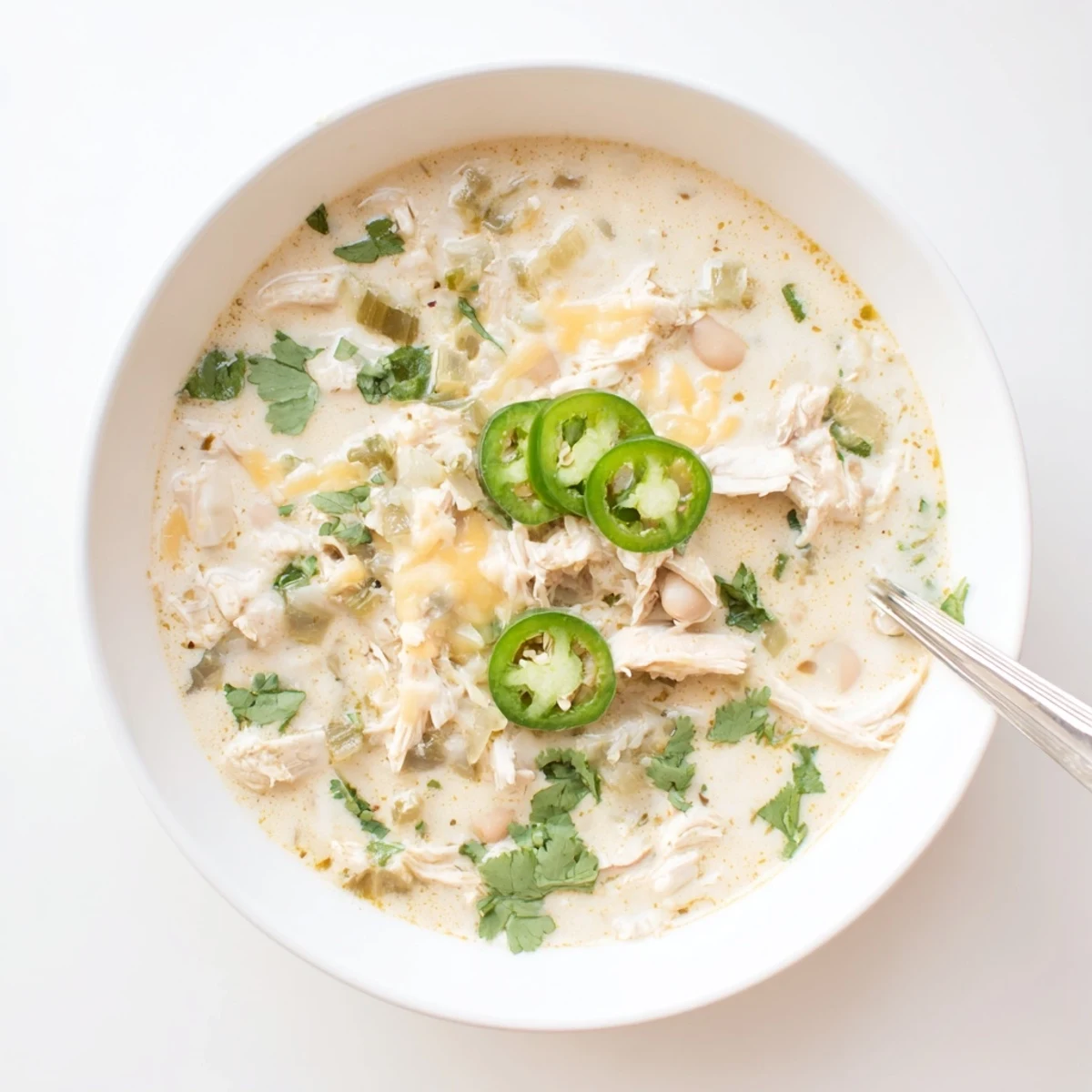 Spoonful of cheesy keto white chicken chili featuring heavy cream, spices, and succulent chicken pieces