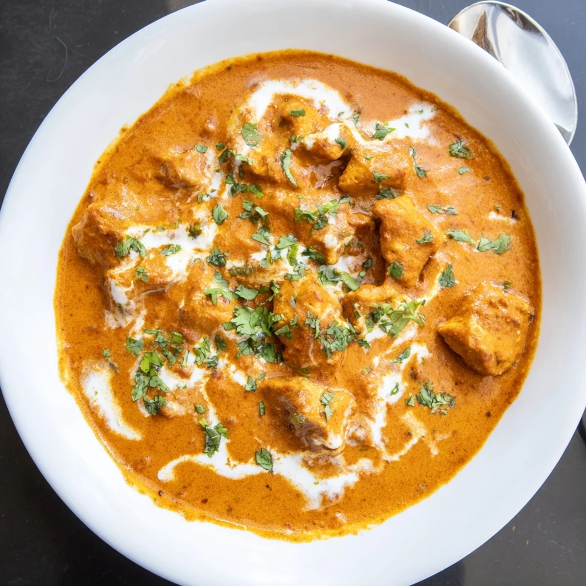 Homemade butter chicken featuring golden brown chicken thighs in a velvety spiced curry sauce topped with chopped cilantro.