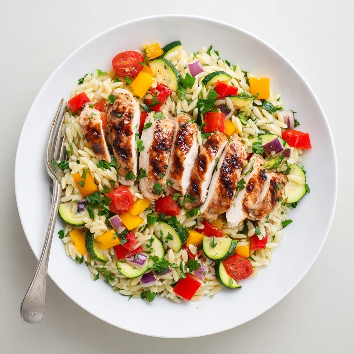 Tender glazed chicken paired with zucchini peppers and cherry tomatoes over herb-seasoned orzo