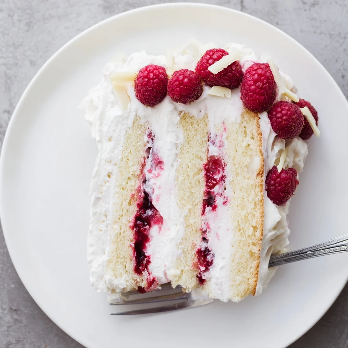 Elegant layered white chocolate raspberry cream cake topped with whipped cream and fresh red raspberries