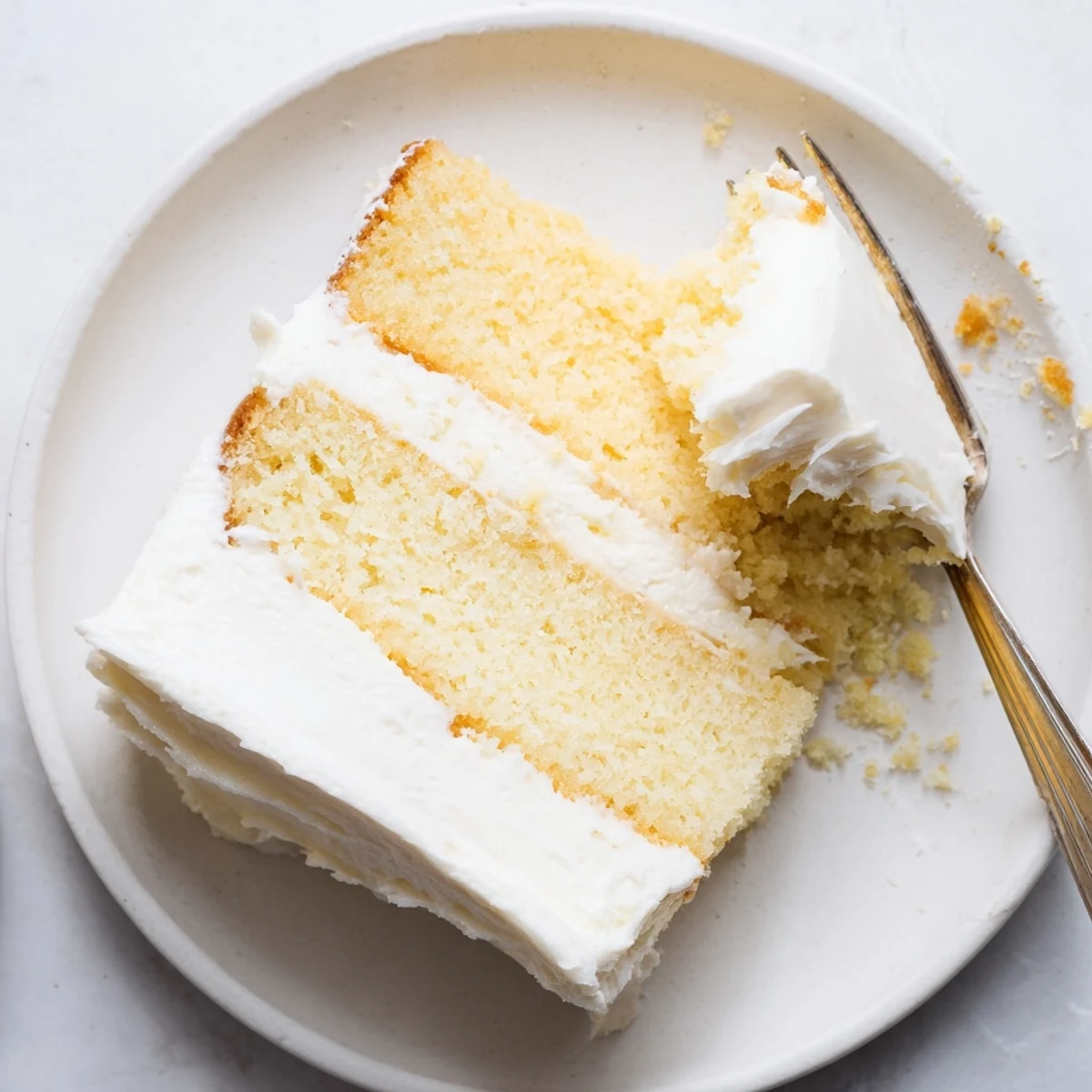 Golden vanilla church cake slice with creamy white frosting on a decorative plate