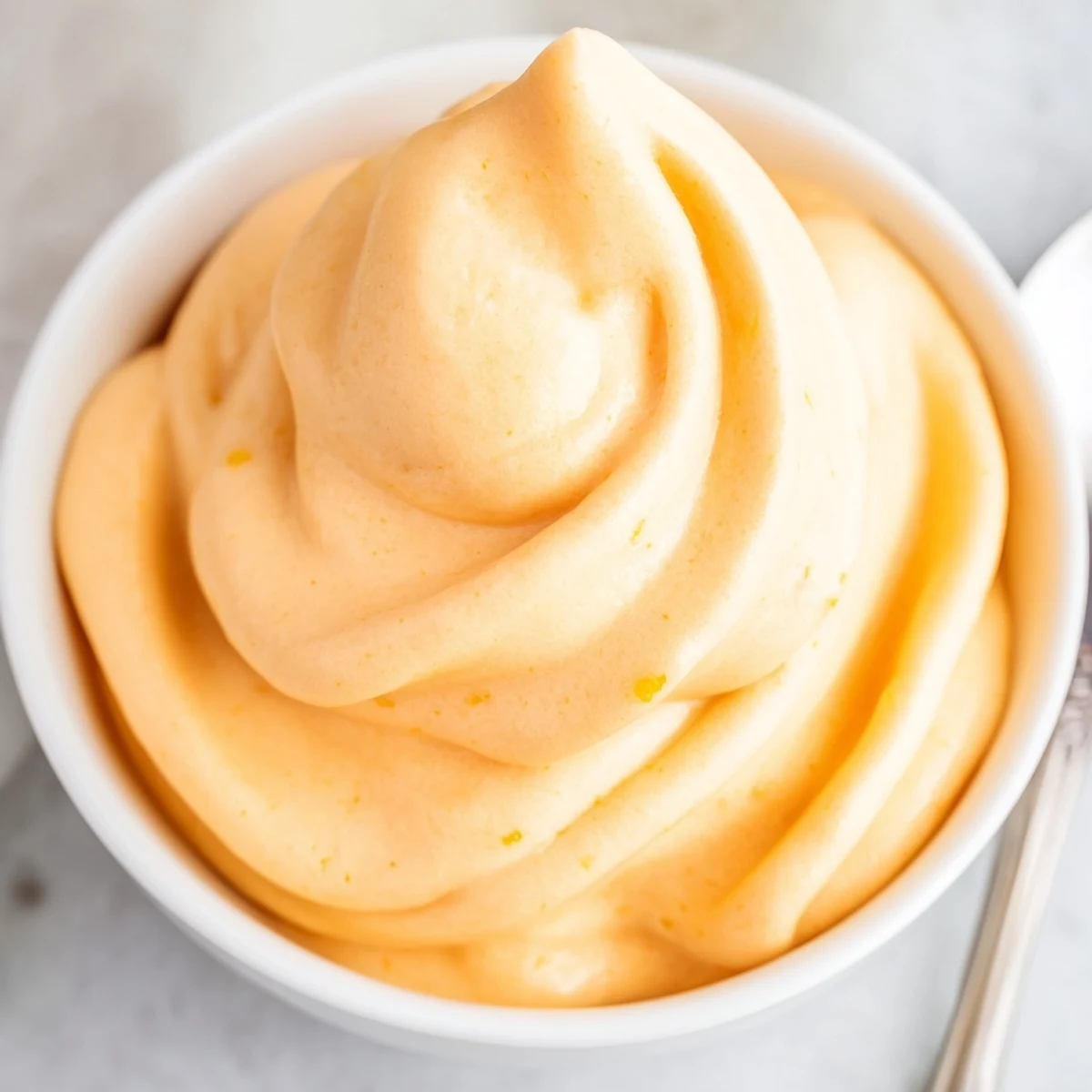 Frosty bowl of homemade orange Dole Whip topped with juicy pineapple chunks and mint leaf