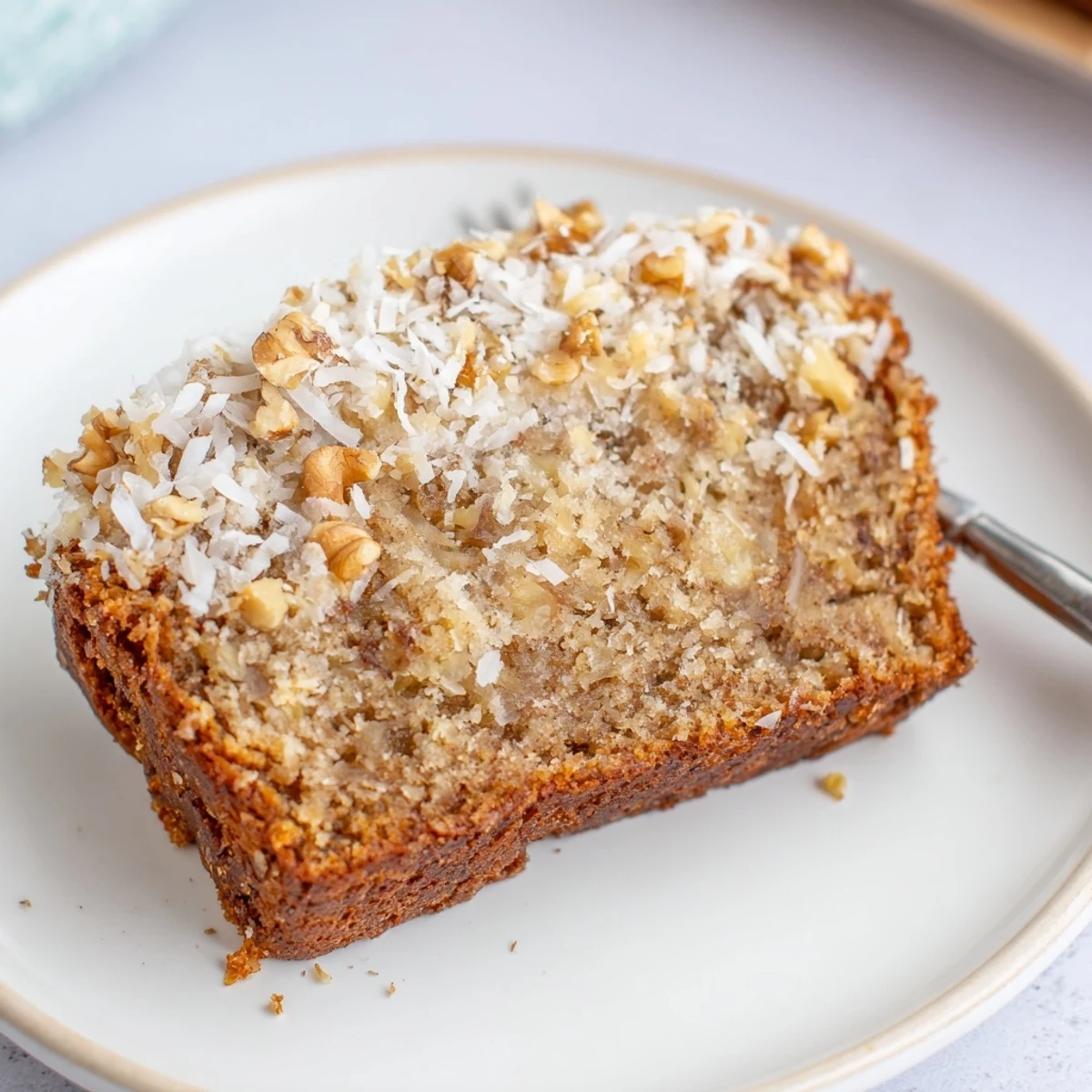 Slice of warm coconut pineapple banana bread with visible fruit pieces and nuts on wooden board