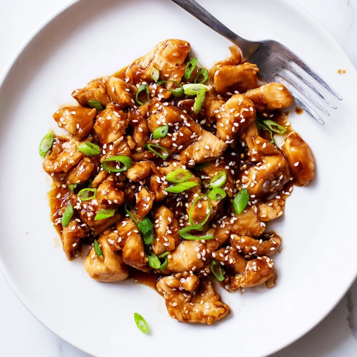 Shredded chicken pieces coated in thick teriyaki glaze with sesame seeds and green onions