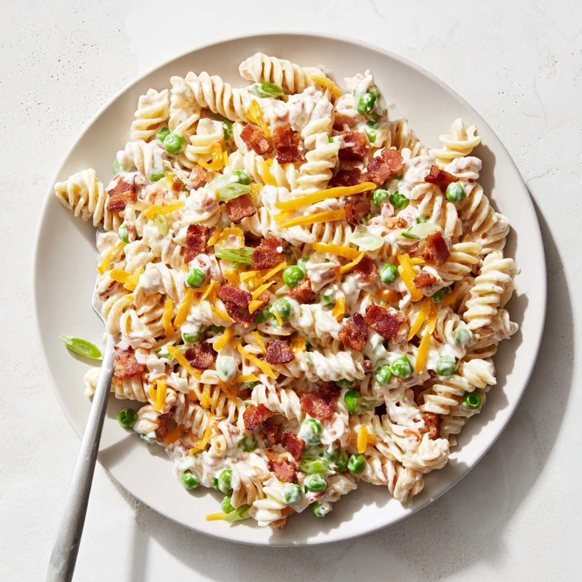 Cold pasta salad bowl topped with crumbled bacon, sharp cheddar, and sweet peas for easy summer side dish