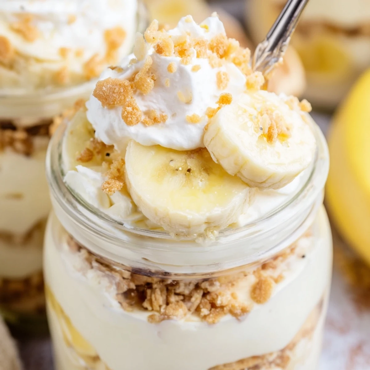 Individual no bake banana pudding cheesecake cups topped with golden wafer crumbs and ripe bananas