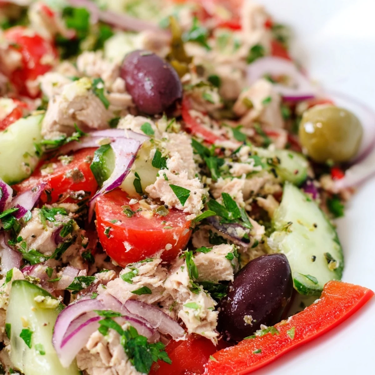Mediterranean tuna salad in a white bowl with cherry tomatoes, cucumber, olives, and fresh parsley