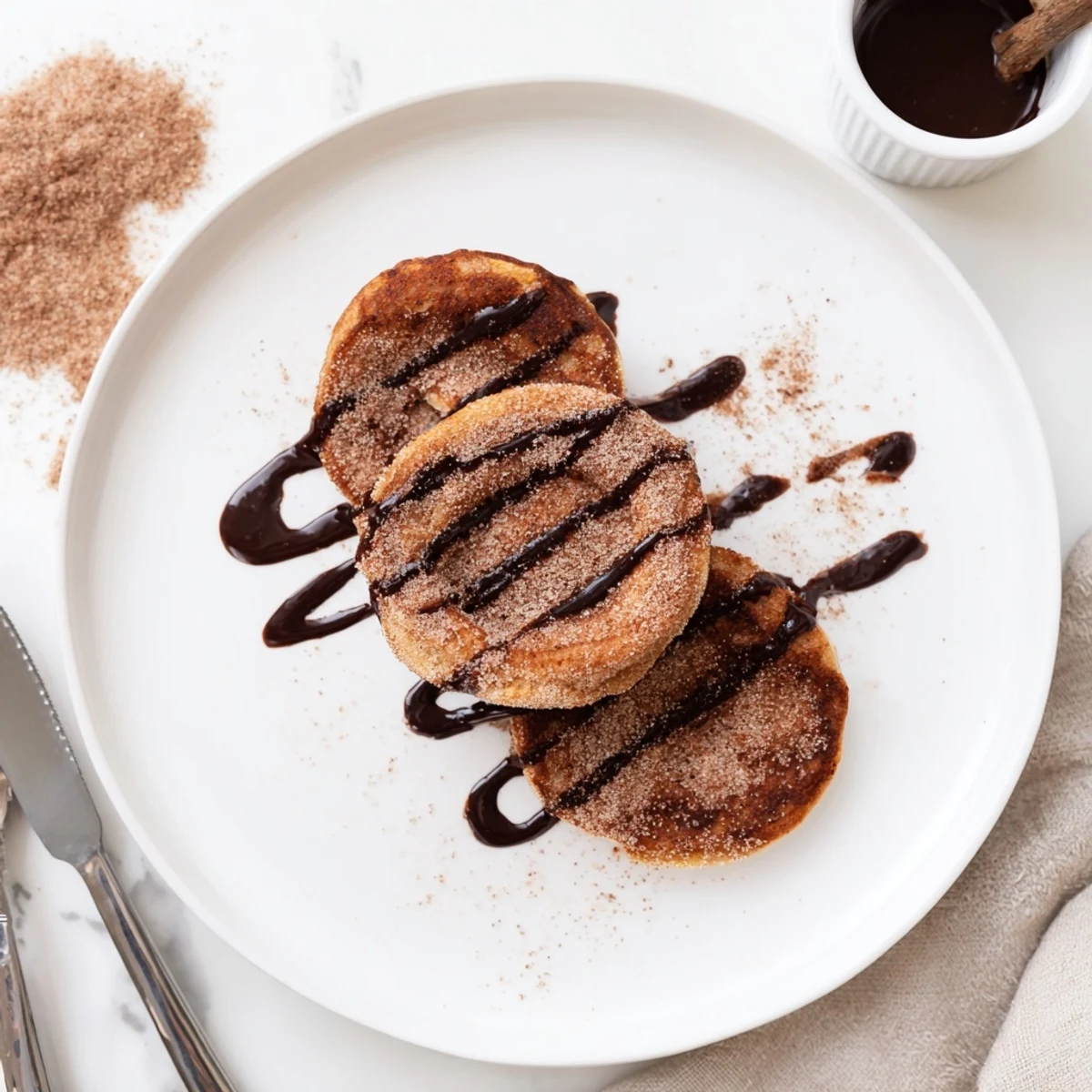 Golden Spanish Churro Pancakes stacked high with rich chocolate sauce drizzled on top