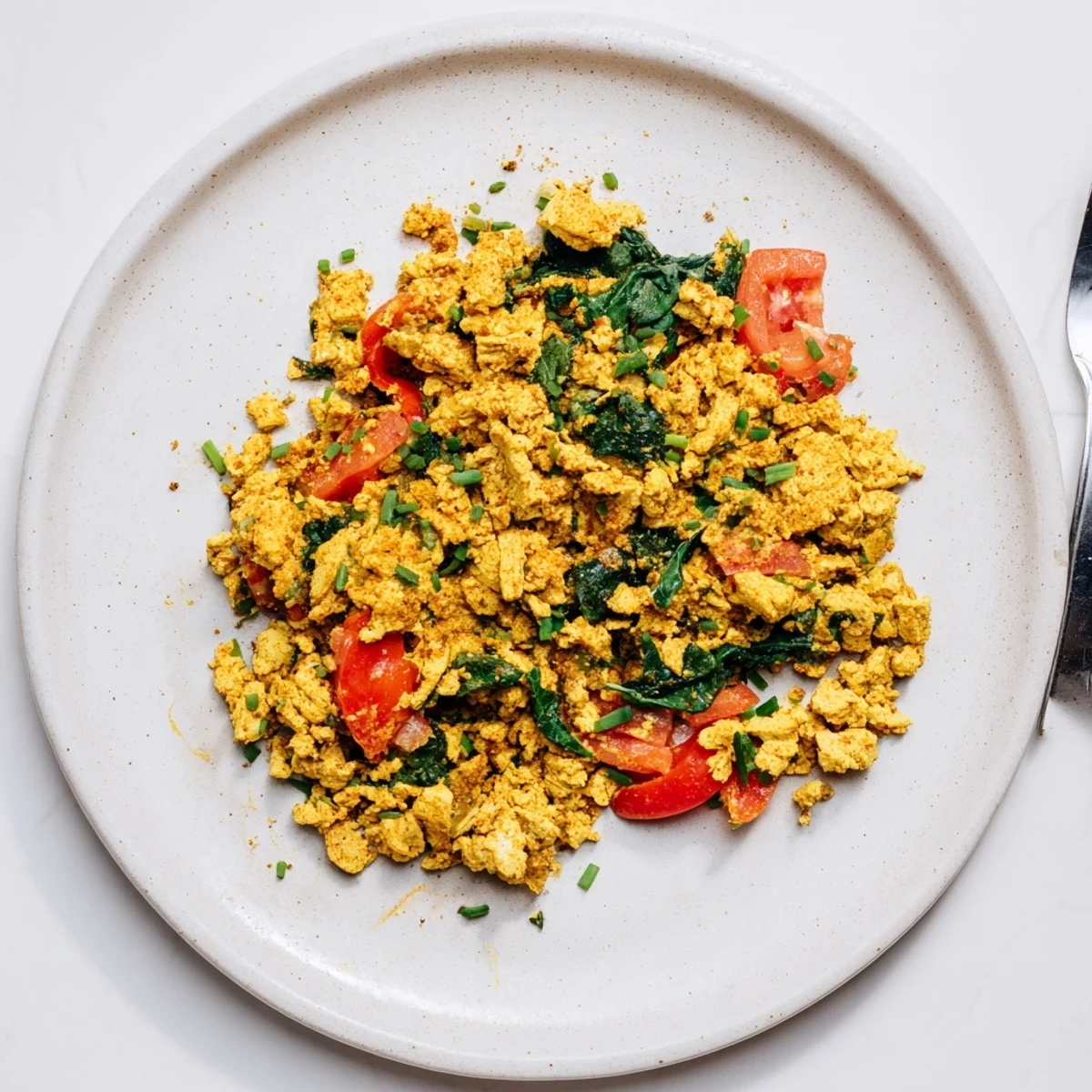 A fluffy, turmeric-hued Tofu Scramble topped with chives and ripe avocado