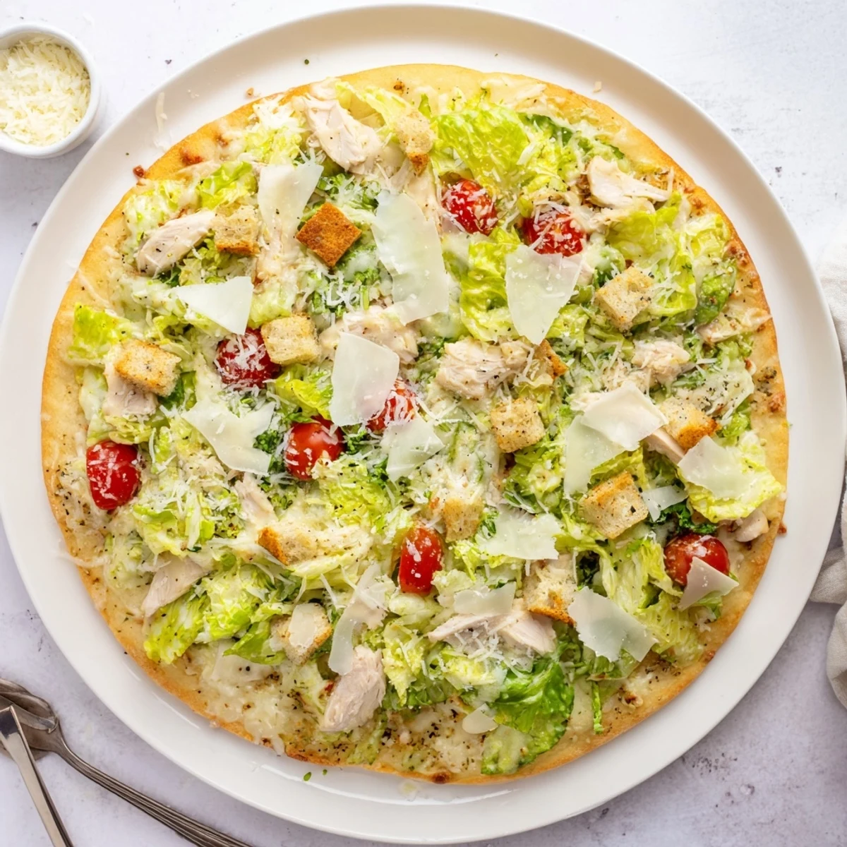 Sliced chicken Caesar salad pizza featuring crisp romaine, croutons, and melted cheese layers