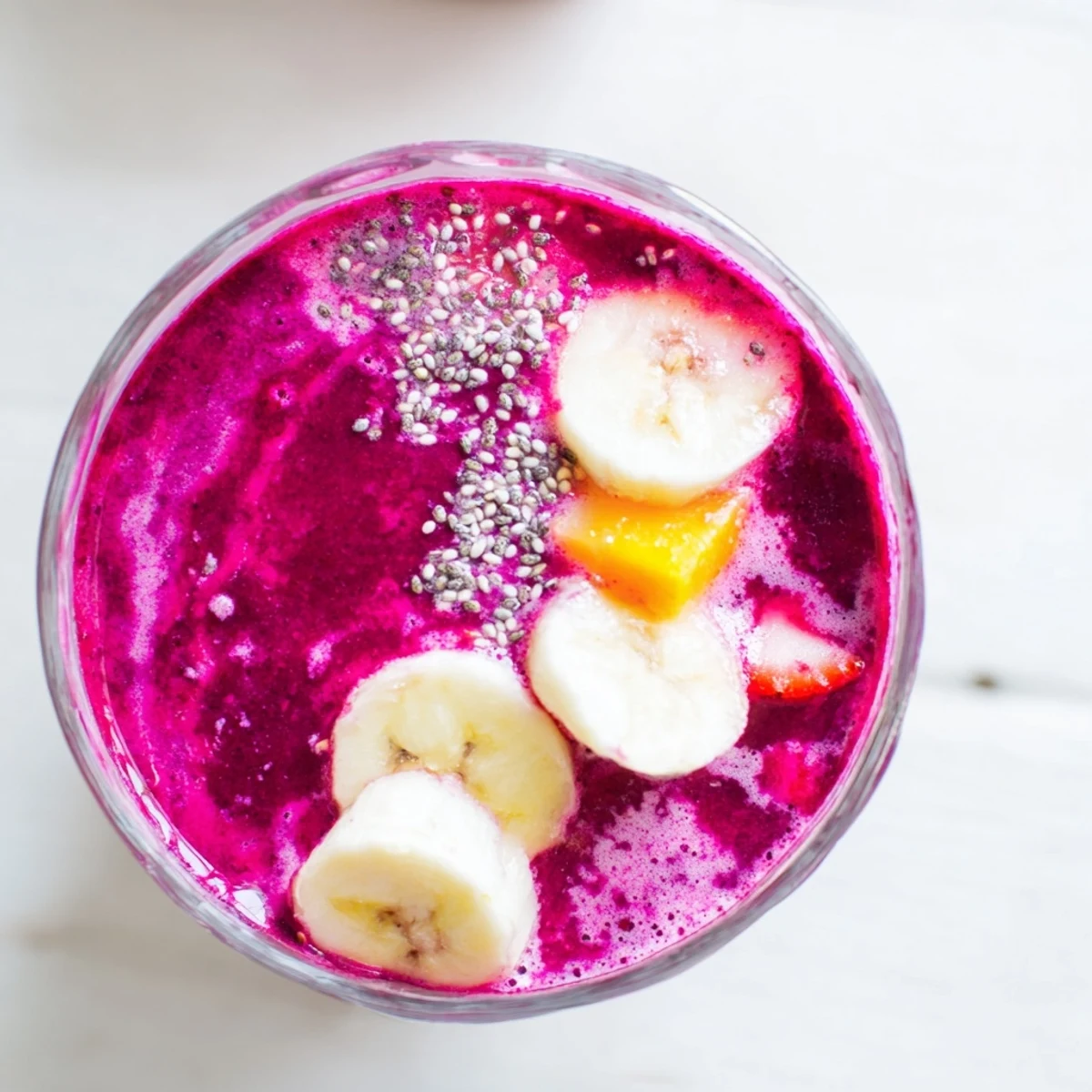 Glossy glass of vibrant pink beet smoothie topped with fresh mint leaves on a wooden table