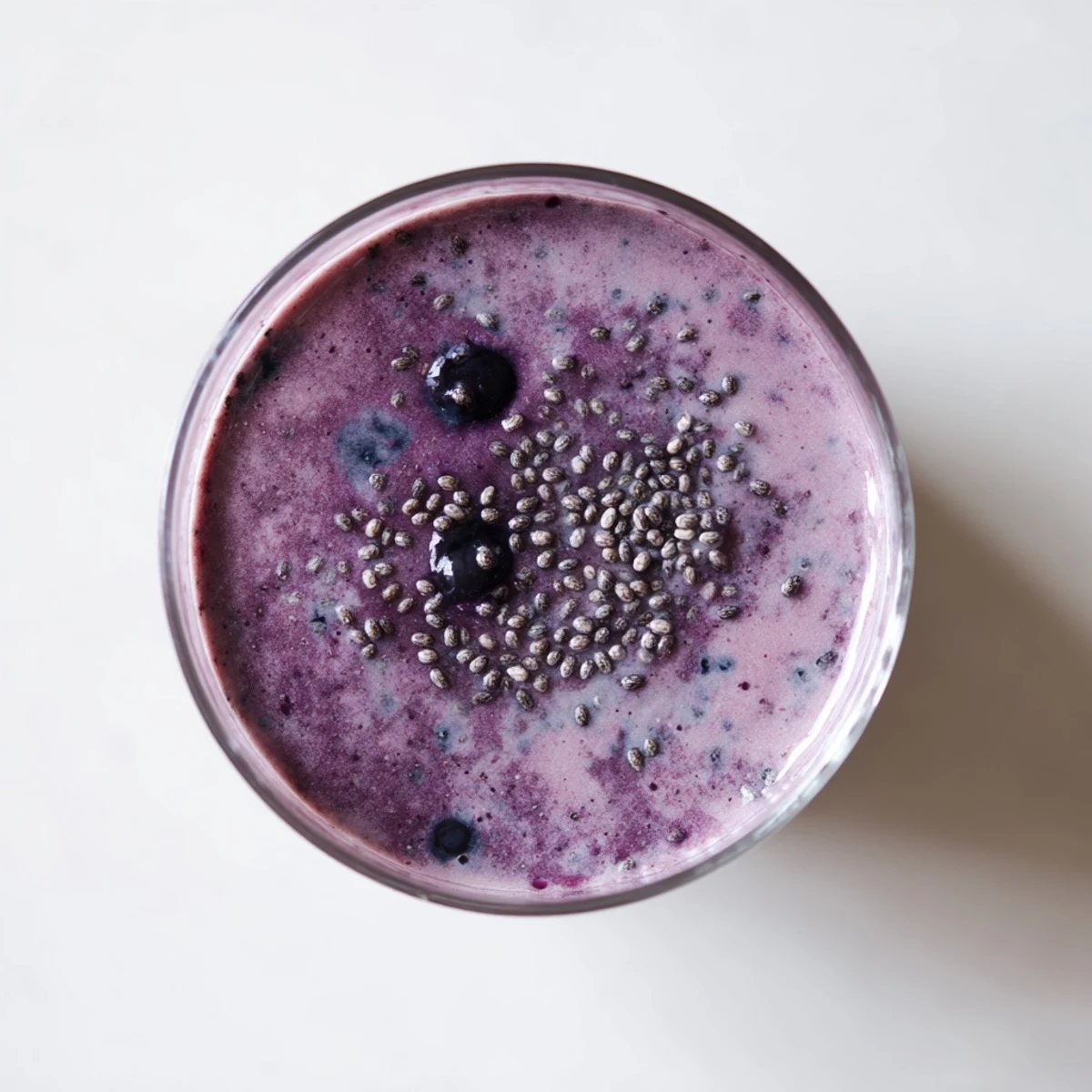 Thick purple chia seed smoothie poured into a glass topped with fresh berries