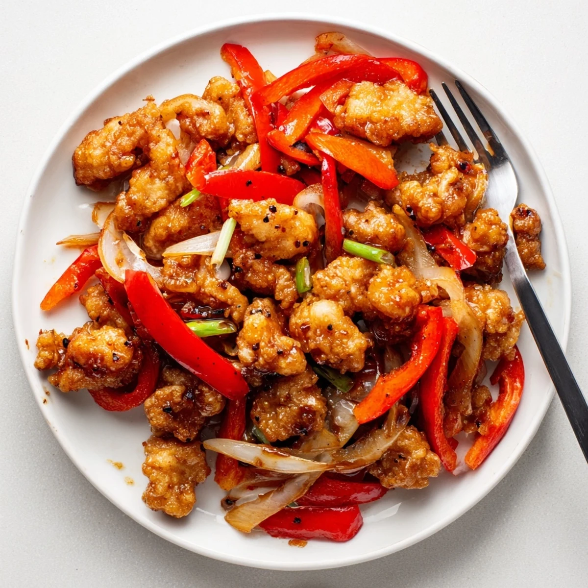 Asian-inspired crispy pepper chicken stir-fry with caramelized onions and red bell pepper slices