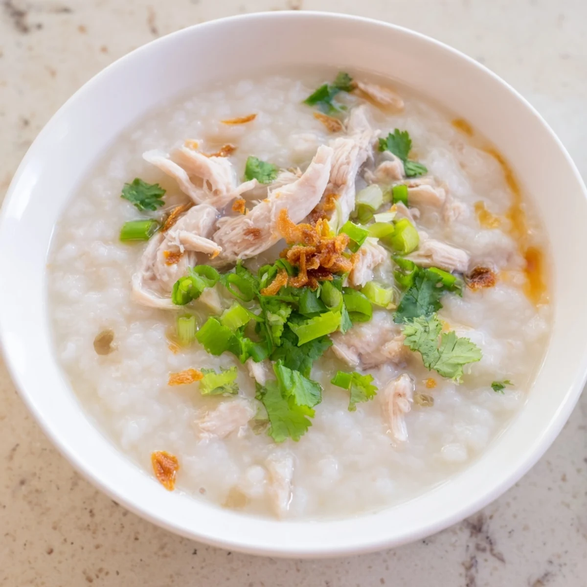 Creamy chicken congee topped with fresh scallions and drizzled with sesame oil in a white bowl