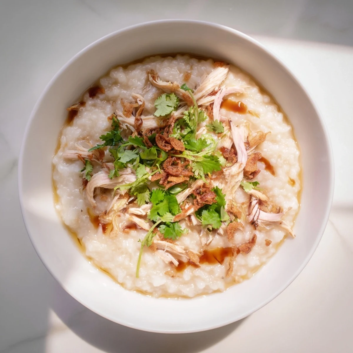 Comforting Chinese chicken congee porridge simmered with ginger and garnished with cilantro and fried shallots