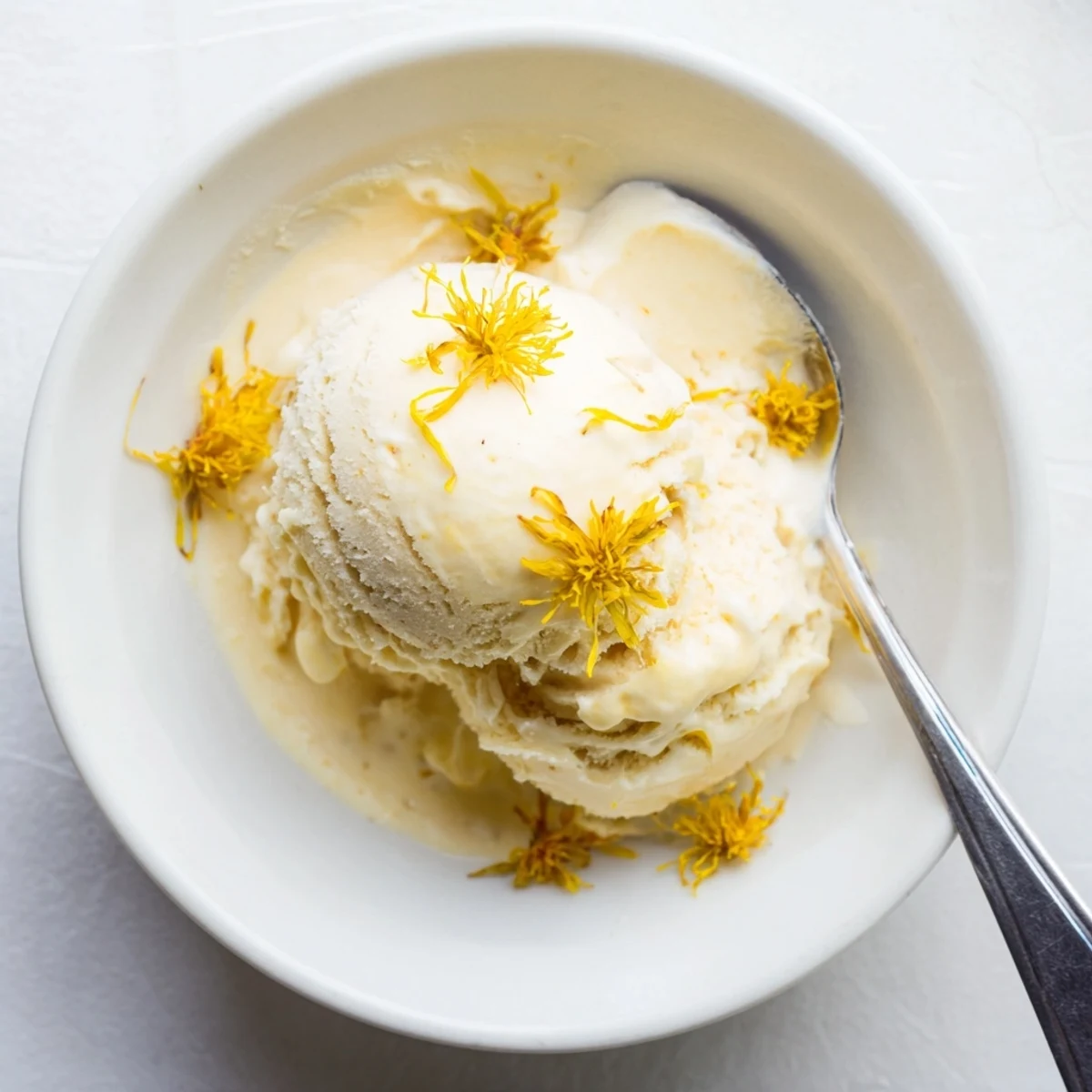 Golden scoops of floral dandelion honey ice cream garnished with fresh yellow dandelion petals on a chilled dessert plate