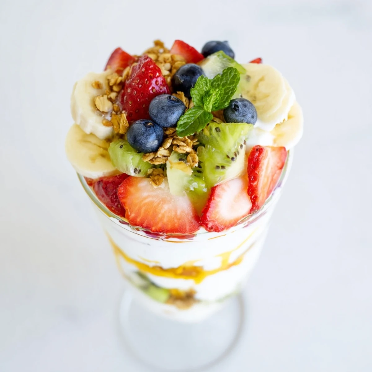 Glass parfait cup showcasing creamy Greek yogurt layered with colorful mixed fruits and golden honey topping