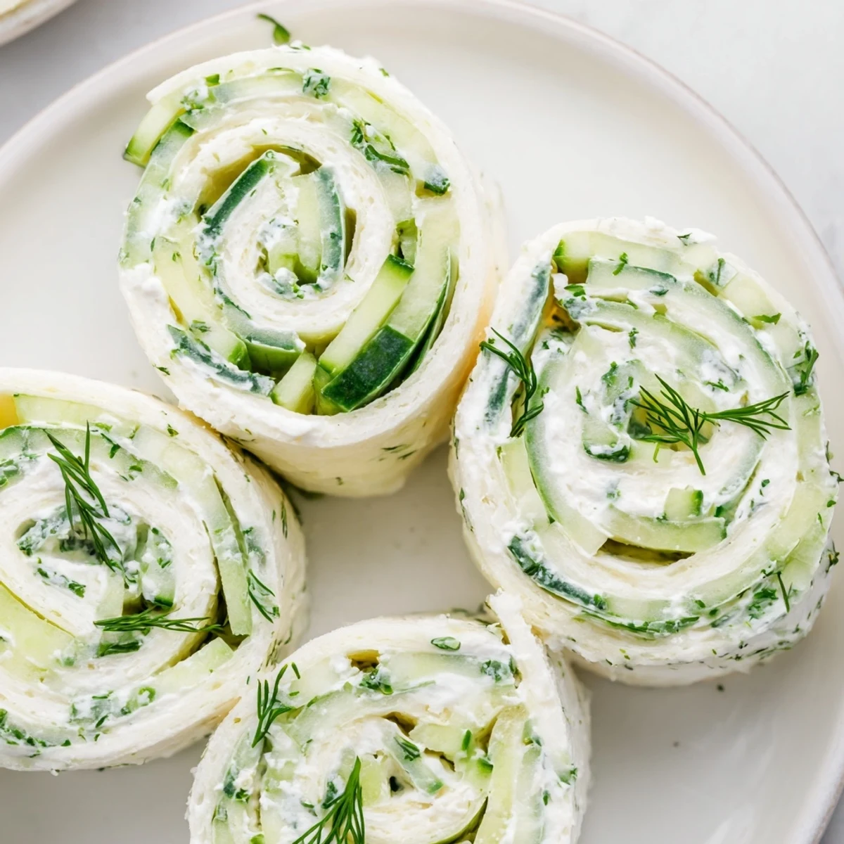 Cucumber And Dill Pinwheels arranged on platter, creamy filling and fresh dill.