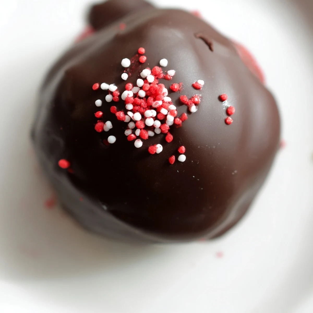Bite-sized red velvet cheesecake balls coated in smooth dark chocolate topped with festive sprinkles