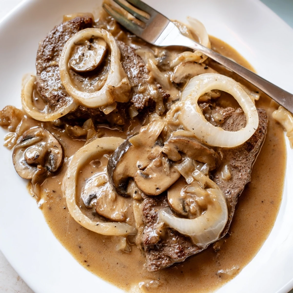 Golden brown country style smothered cube steak swimming in savory brown gravy with sliced onions