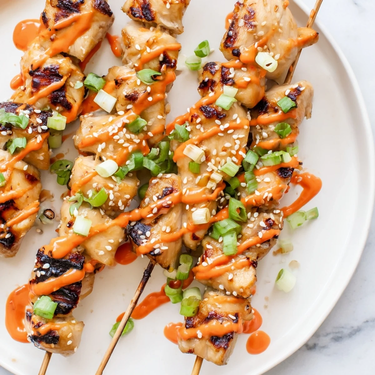 Crispy charred Bang Bang Chicken Skewers topped with sesame seeds and spring onions
