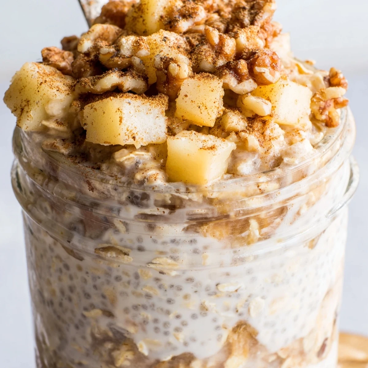 Creamy apple crumble overnight oats layered in a jar with cinnamon apples and crunchy walnut topping