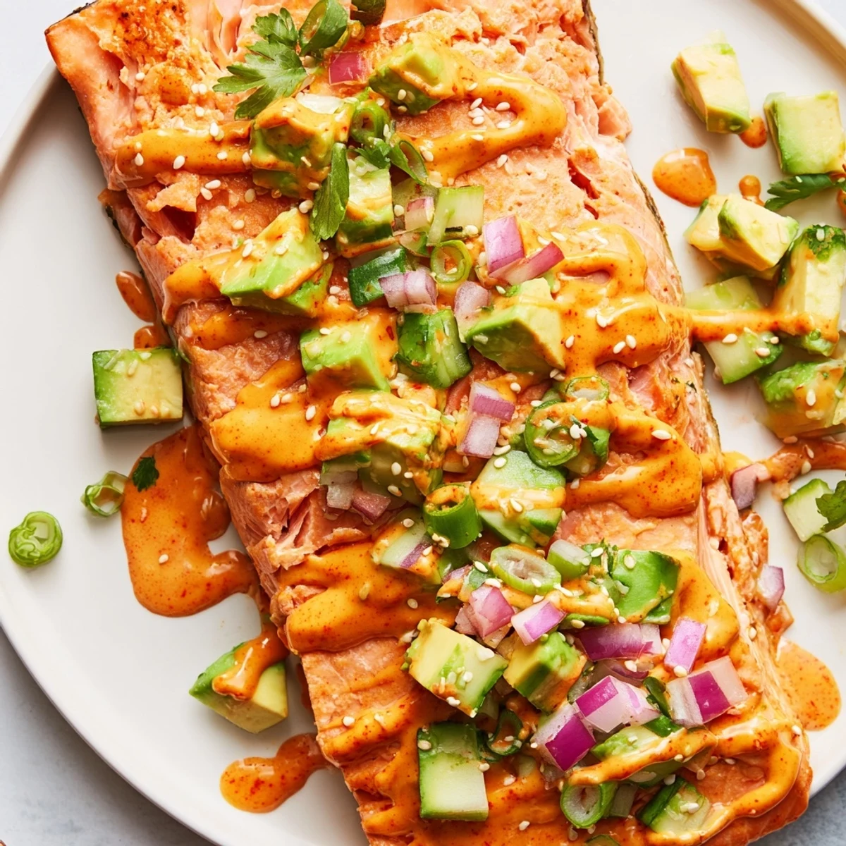 Golden Bang Bang Salmon fillets topped with creamy sauce over cool avocado cucumber relish