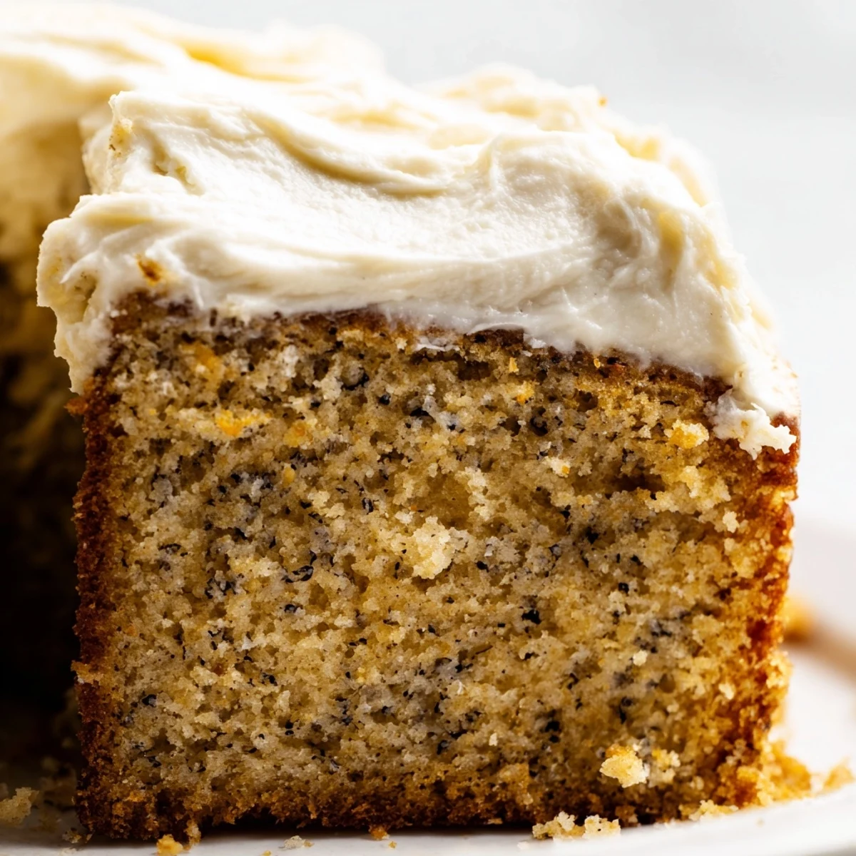 Slice of brown butter banana cake with thick cream cheese frosting on a rustic plate