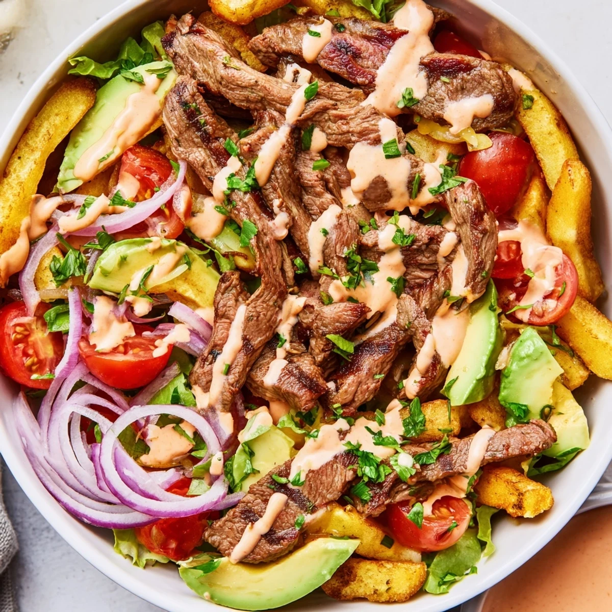 A steak strips and crispy fries bowl drizzled with smoky sauce and fresh vegetables