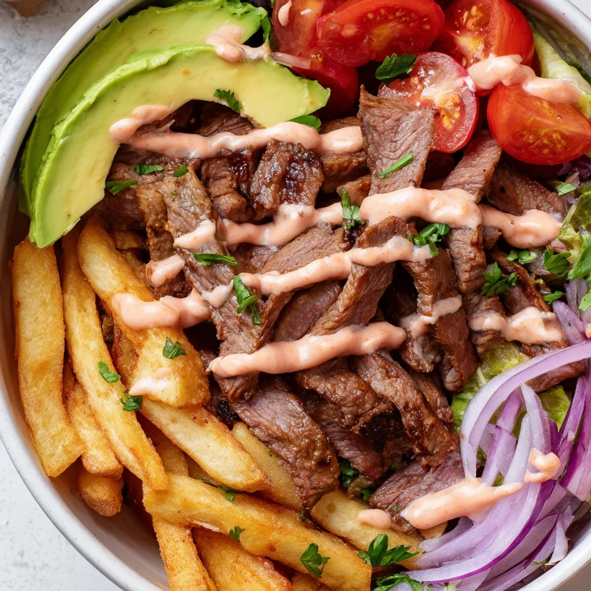 Steak strips and crispy fries bowl loaded with cherry tomatoes, greens, and zesty mustard sauce