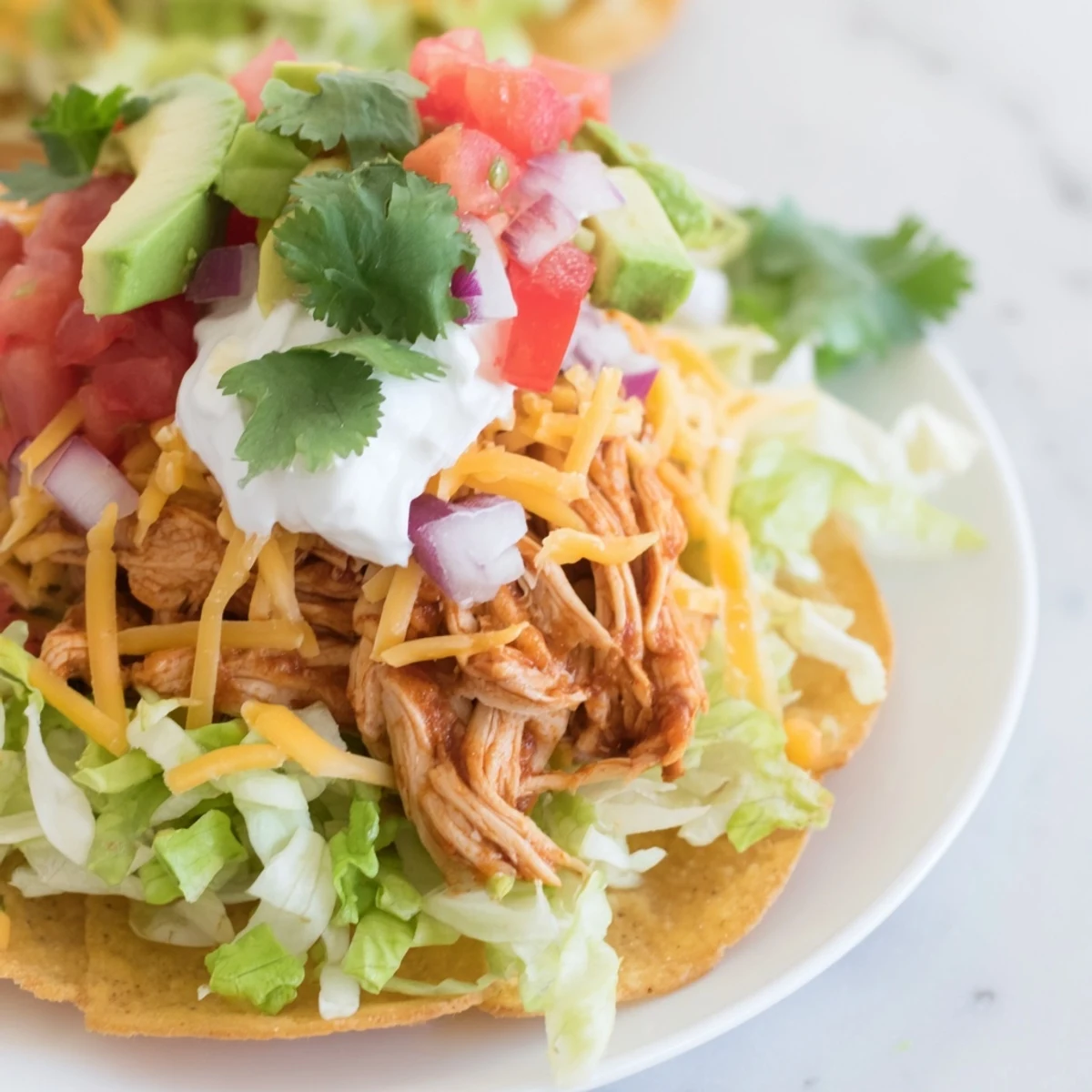 Golden chicken tostadas topped with fresh lettuce, tomatoes, and creamy avocado slices.  