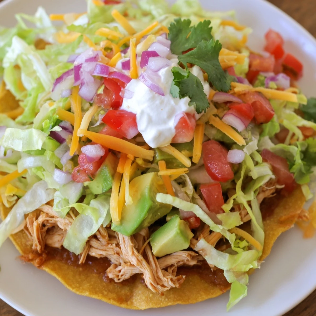 Ultimate Chicken Tostadas piled high with beans, juicy meat, and sour cream.