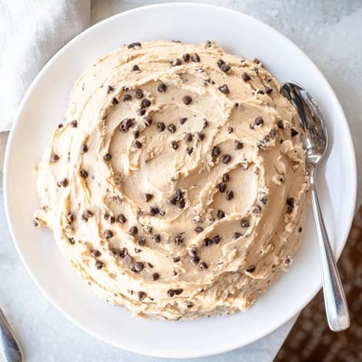 A bowl of Cookie Dough Frosting beside cupcakes, showing its soft, edible cookie dough texture.