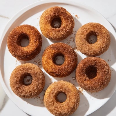 Golden Delicious Baked Cinnamon Sugar Donuts You Can’t Resist are arranged on a plate beside a steaming mug of coffee.