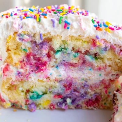 Unicorn Poke Cake sliced to reveal vibrant pudding layers under confetti sprinkles